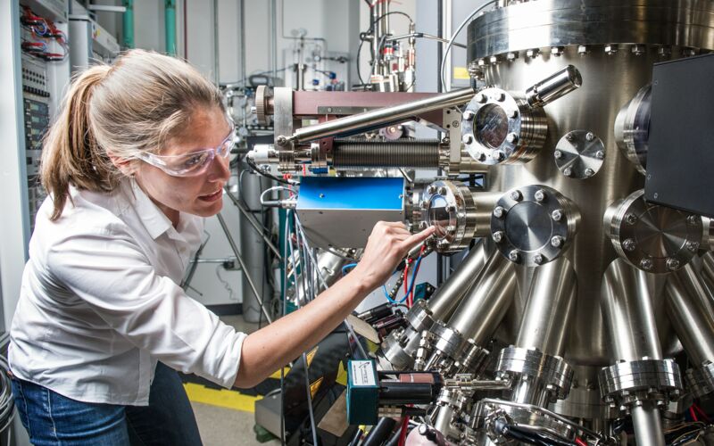 Frau mit Schutzbrille begutachtet große industrielle Maschine.