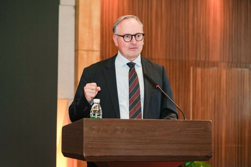 A man in a suit stands in front of a lectern.