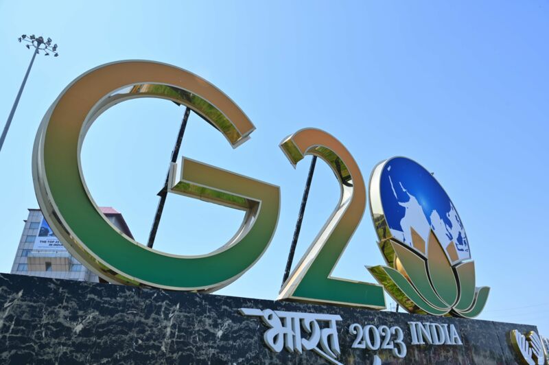A gold-framed lettering with the letters "G20", consisting of the colours green and orange, stands next to the symbol of an earth and a lotus flower above the lettering "India 2023".