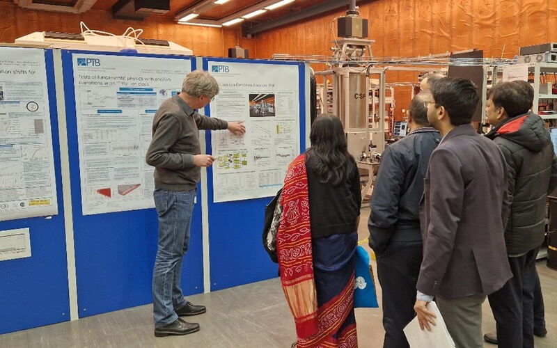 A group of people stand in front of a man who points to a poster he is presenting.