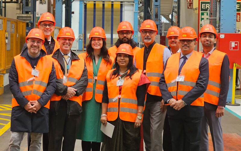 People with orange safety waistcoats and helmets pose in a production hall.