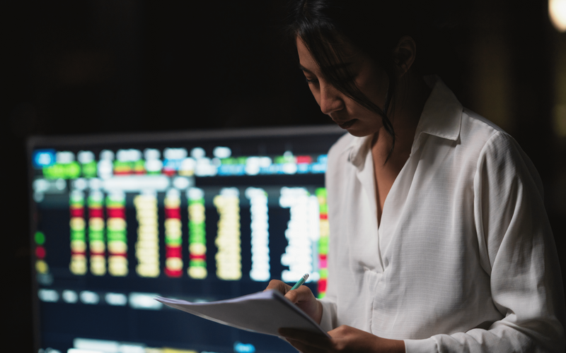 Woman with piece of paper and pencil in front of computers