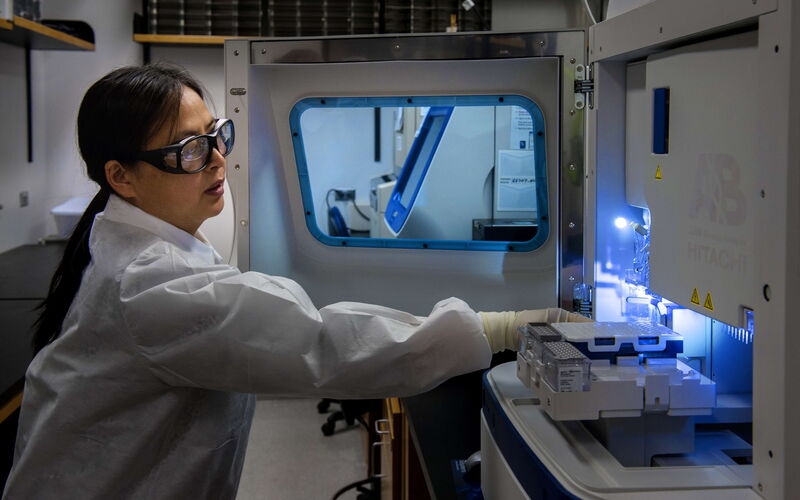 A woman in a laboratory wearing protective gear maintaining an instrument.